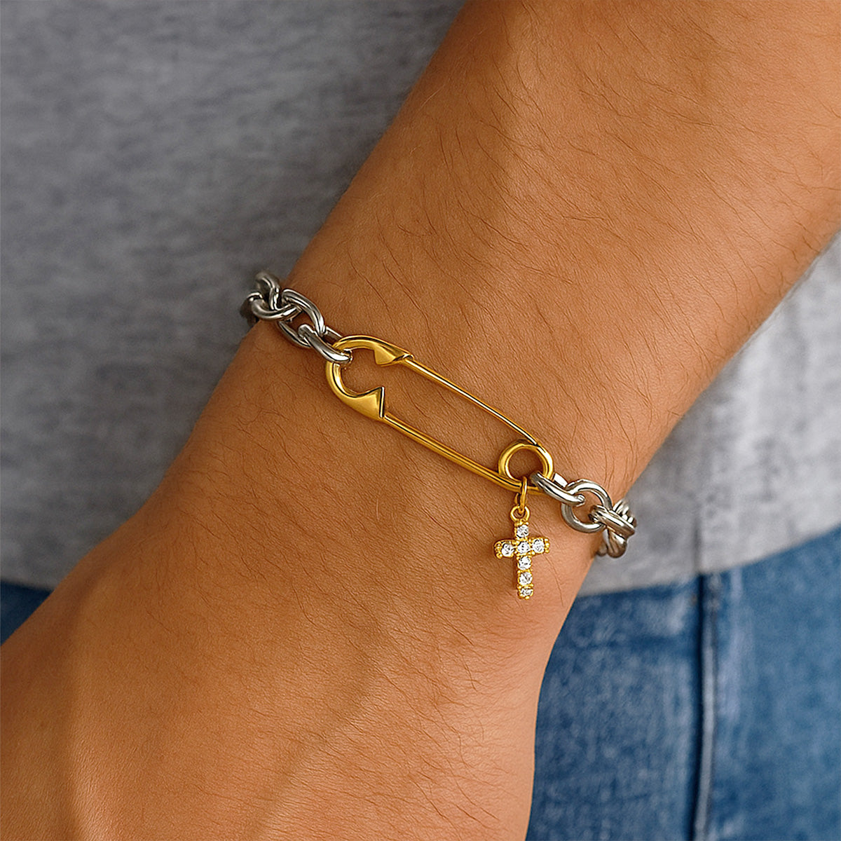 Close-up of a stainless steel safety pin link bracelet featuring a studded cross pendant with zircon stones, highlighting the durability of pvd gold plated jewelry for men.