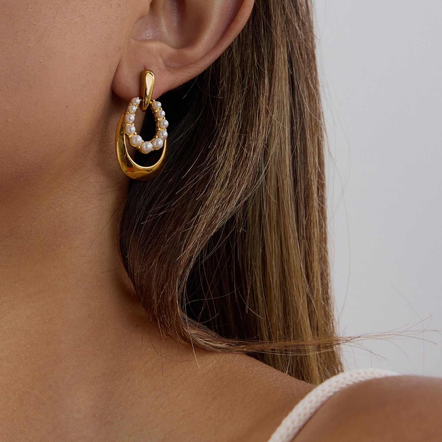 Woman wearing stainless steel pearl earrings with a modern oval drop design. These pvd gold plated titanium stud earrings are hypoallergenic, non tarnish, and non shedding—perfect for daily wear.