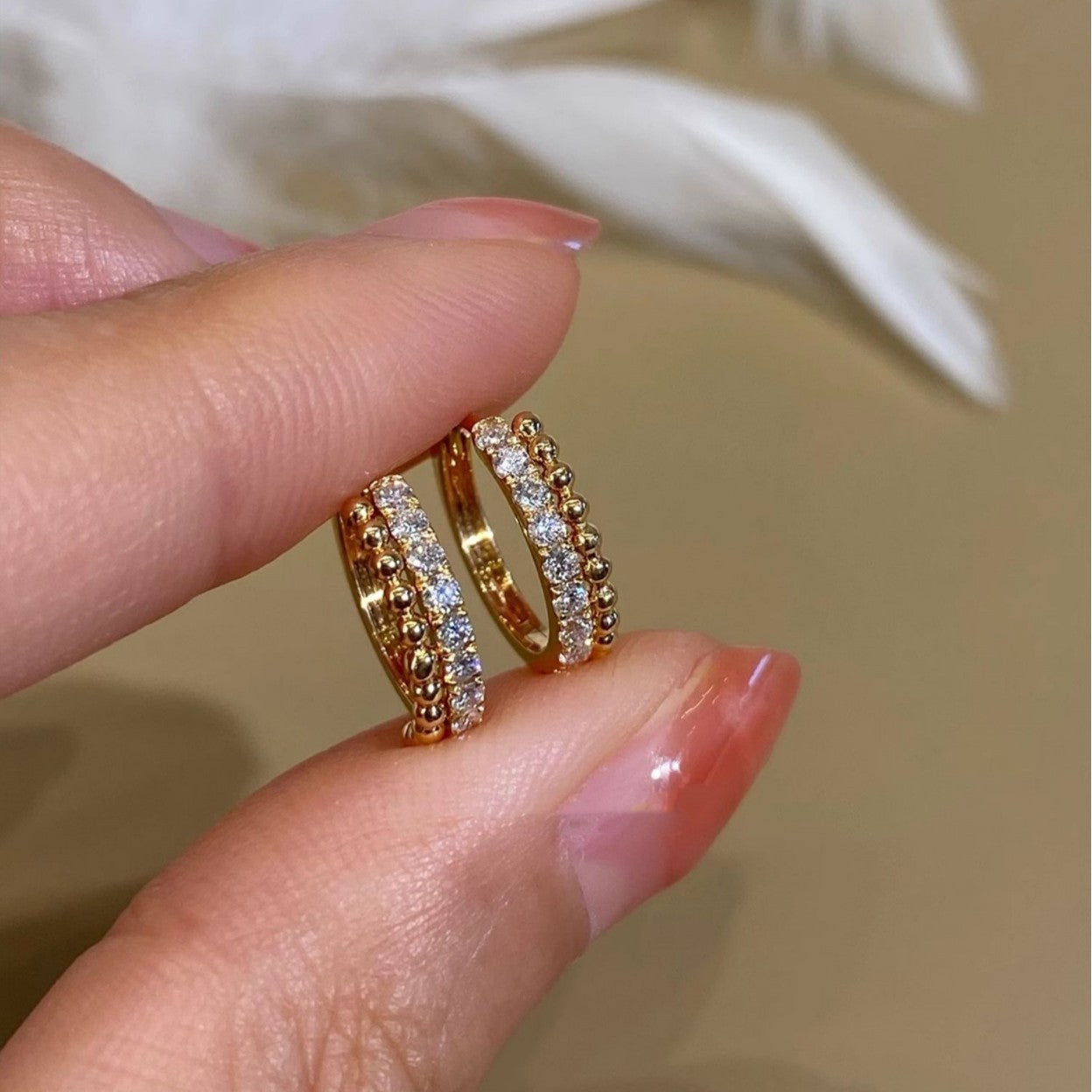Hand holding two 18k gold plated cubic zirconia beaded huggie hoops, 925 sterling silver earrings wholesale supplier.