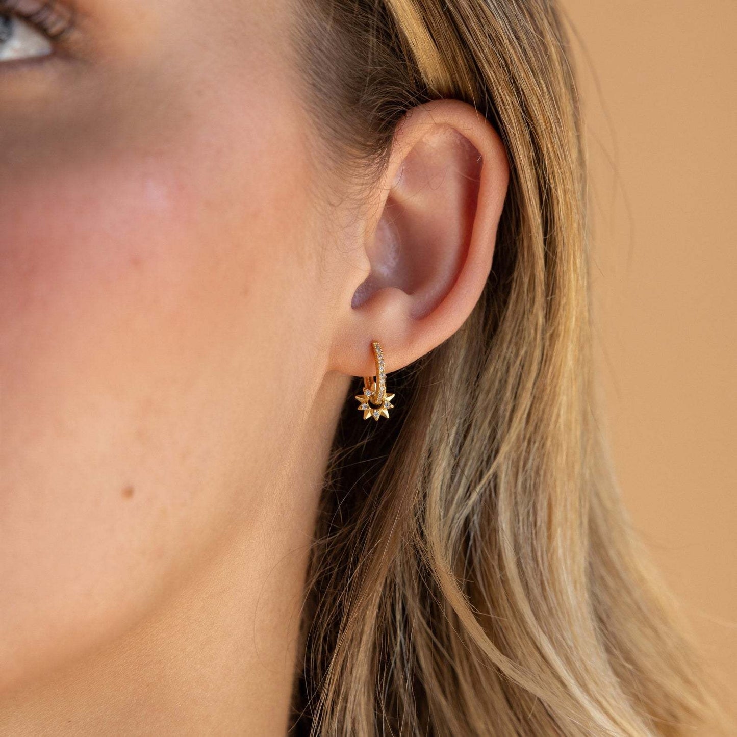 S925 celestial star huggie earrings with sparkling cubic zirconia, displayed flat on a marble surface with festive props