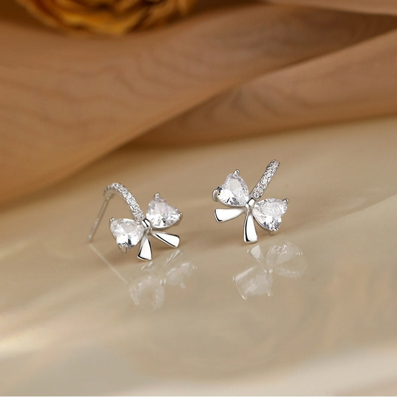 Sterling silver bow-shaped stud earrings with heart-cut cubic zirconia stones, perfect as an elegant gift for women