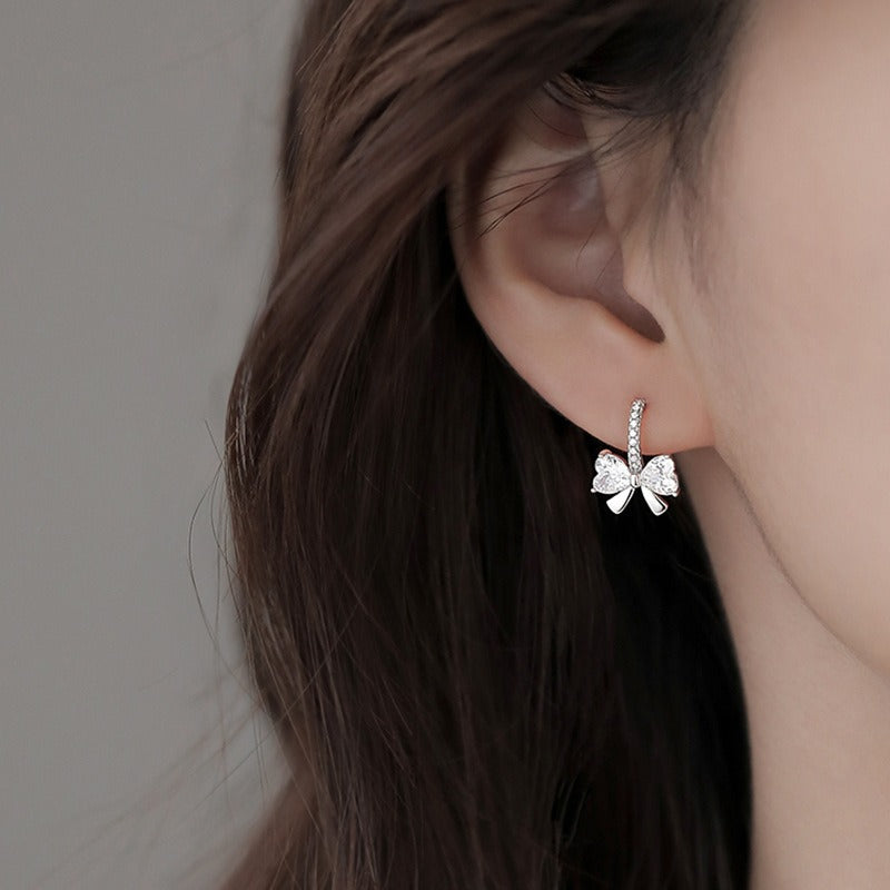 Dainty cubic zirconia bow earrings in sterling silver, reflecting soft light and ideal for everyday elegance