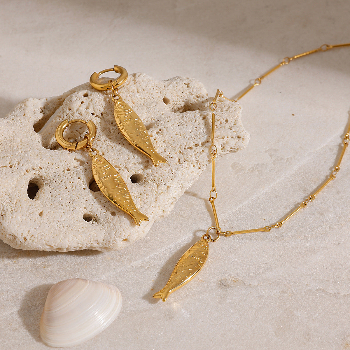 Close-up of 18k gold plated earrings with fish pendants, part of a stainless steel matching jewelry set. Perfect for summer beach jewelry or vacation jewelry looks.