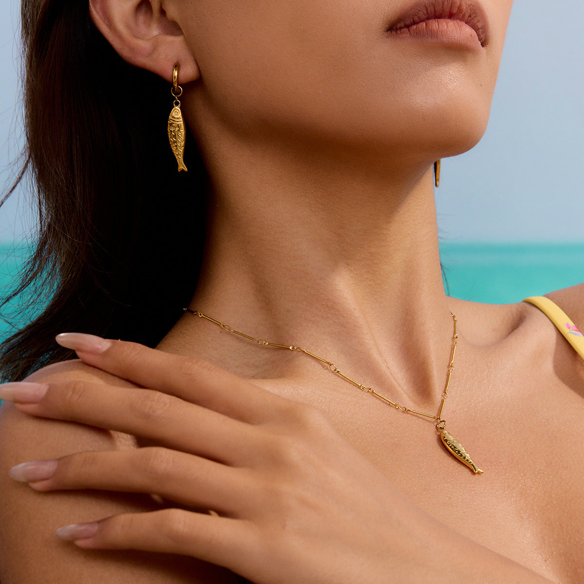 Gold Fish Pendant Necklace laid on a beach-style linen background. A stainless steel necklace with ocean beach style, perfect for vacation jewelry.