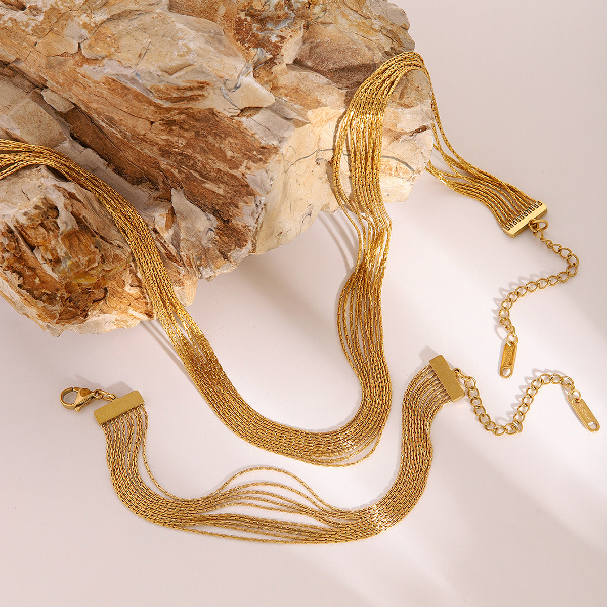 Gold layered chain necklace and bracelet set displayed on beige stone background. This stainless steel jewelry set is ideal as trendy stackable jewelry for girls.