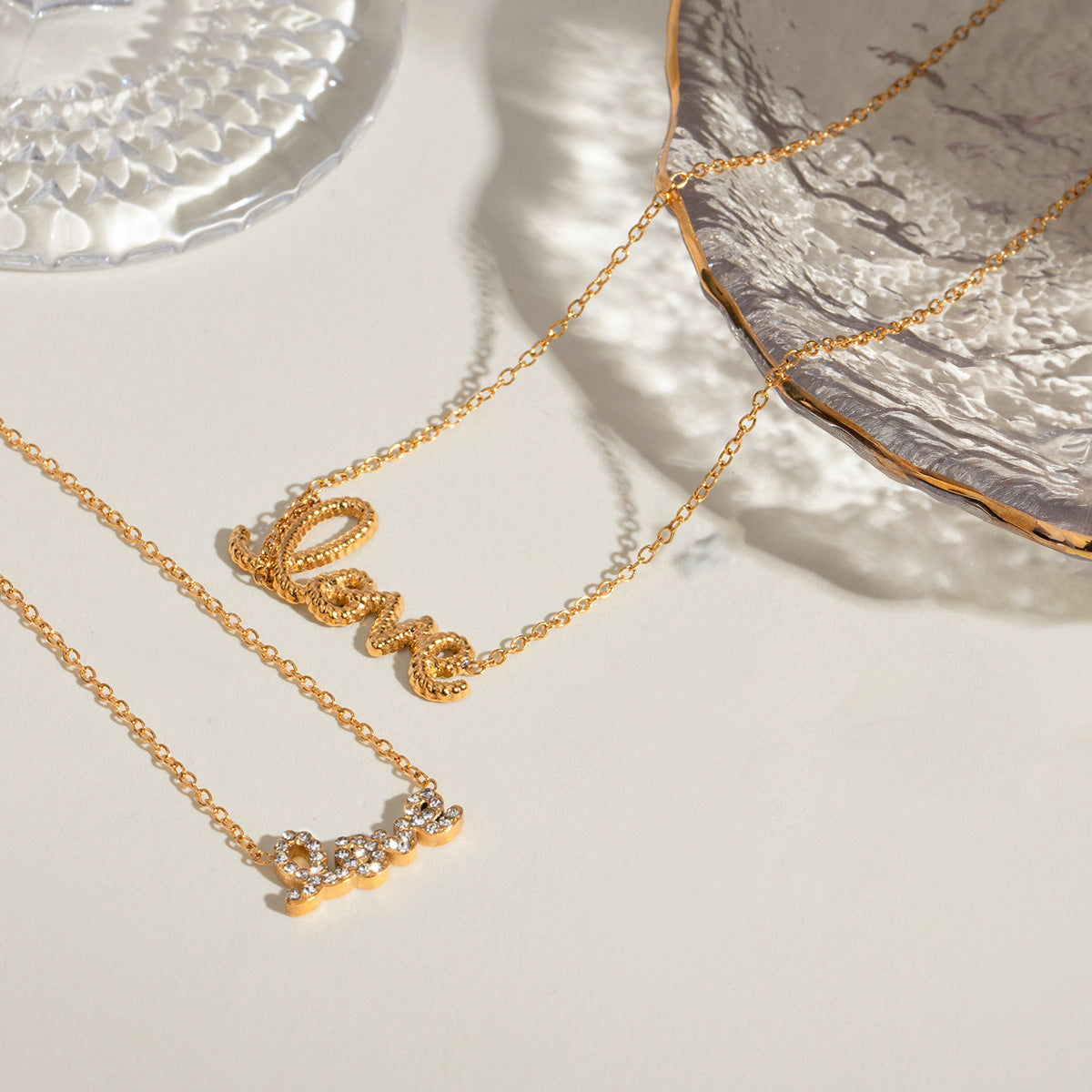 Flat lay showing two styles of gold love necklaces, both featuring the word 'love' in gold — one with cubic zirconia. Ideal for layering, these anti tarnish gold necklaces make perfect Valentine’s Day necklaces for her and stylish gifts