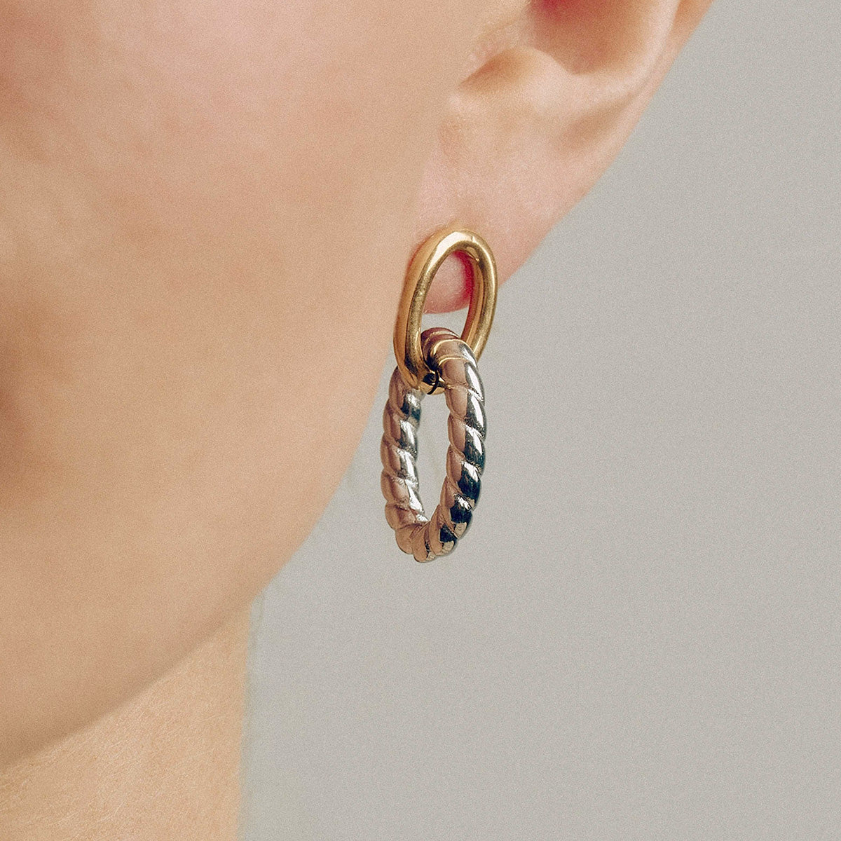 Model wearing chunky oval twist earrings in gold and silver. Two tone stainless steel earrings perfect for women seeking geometric jewelry with hypoallergenic titanium studs. Ideal for wholesale fashion accessories.