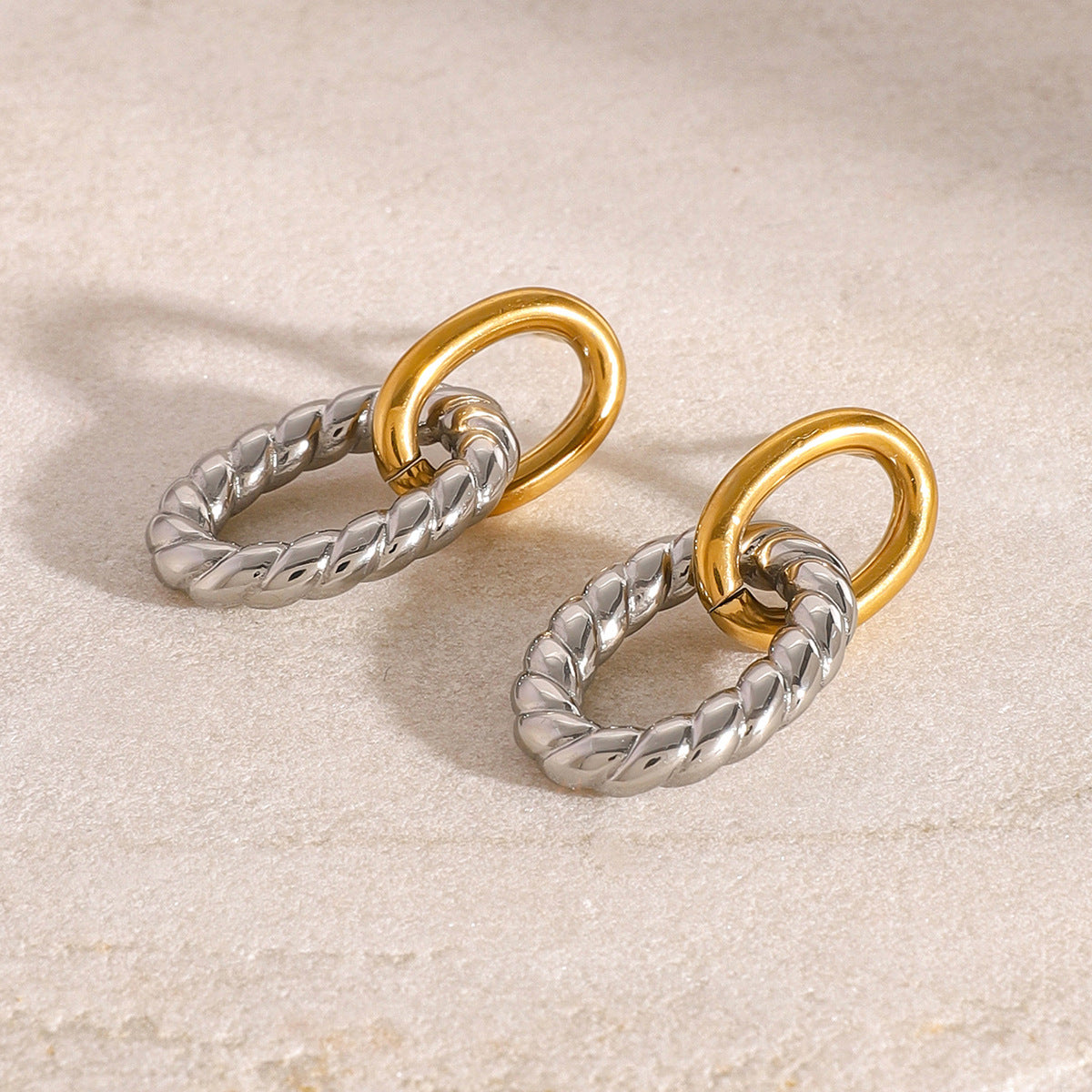 Close-up of two tone oval twist earrings on marble surface. Chunky stainless steel earrings in gold and silver for women, perfect for daily wear or wholesale jewelry collections.