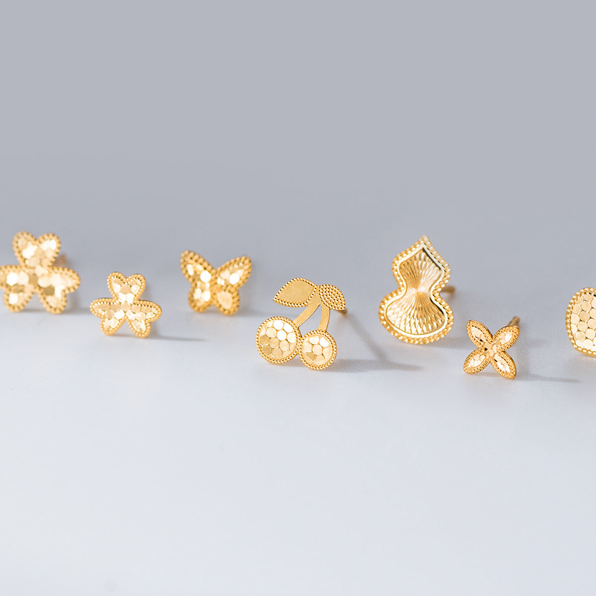 Set of wholesale 925 sterling silver stud earrings in gold including flower, butterfly, cherry, gourd, and heart designs, laser cut hypoallergenic styles.