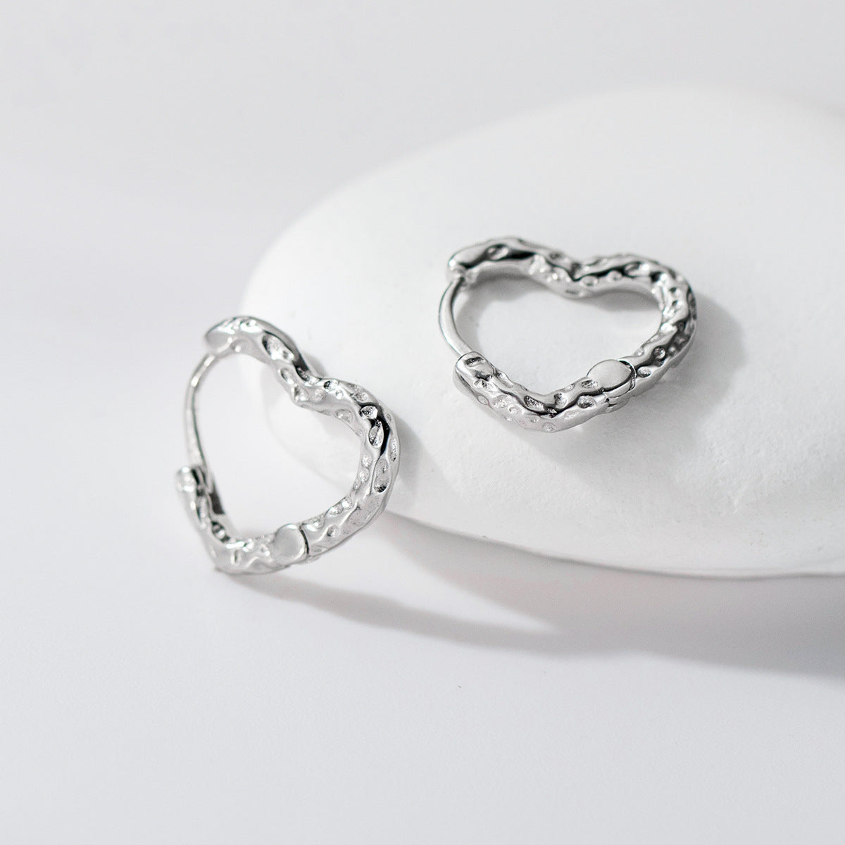 Wholesale silver 925 jewelry textured heart hoop earrings displayed on white stone background