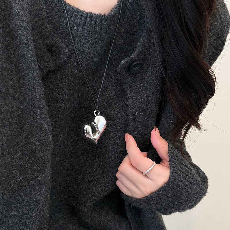 Silver chunky heart pendant necklace styled with a dark knit cardigan.
