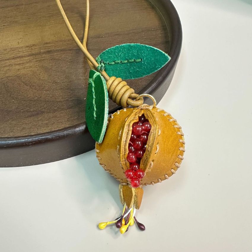 Set of red and yellow genuine leather pomegranate charms hanging on handbag, handmade leather bag charm design perfect for fruit bag charm wholesale, fashion accessories wholesale, and seasonal gift collections.