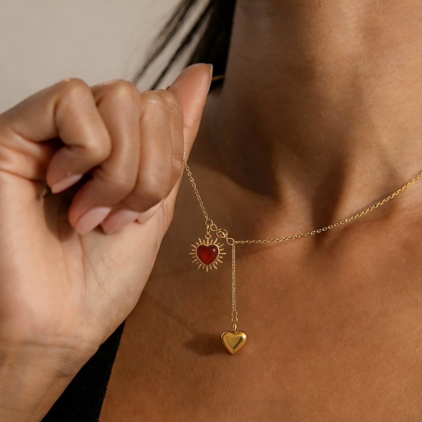 Model wearing gold tone lariat necklace with red agate heart sun charm and heart drop pendant