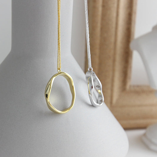 Gold irregular oval pendant necklace displayed on a vase, minimalist jewelry wholesale design for boutiques and retailers