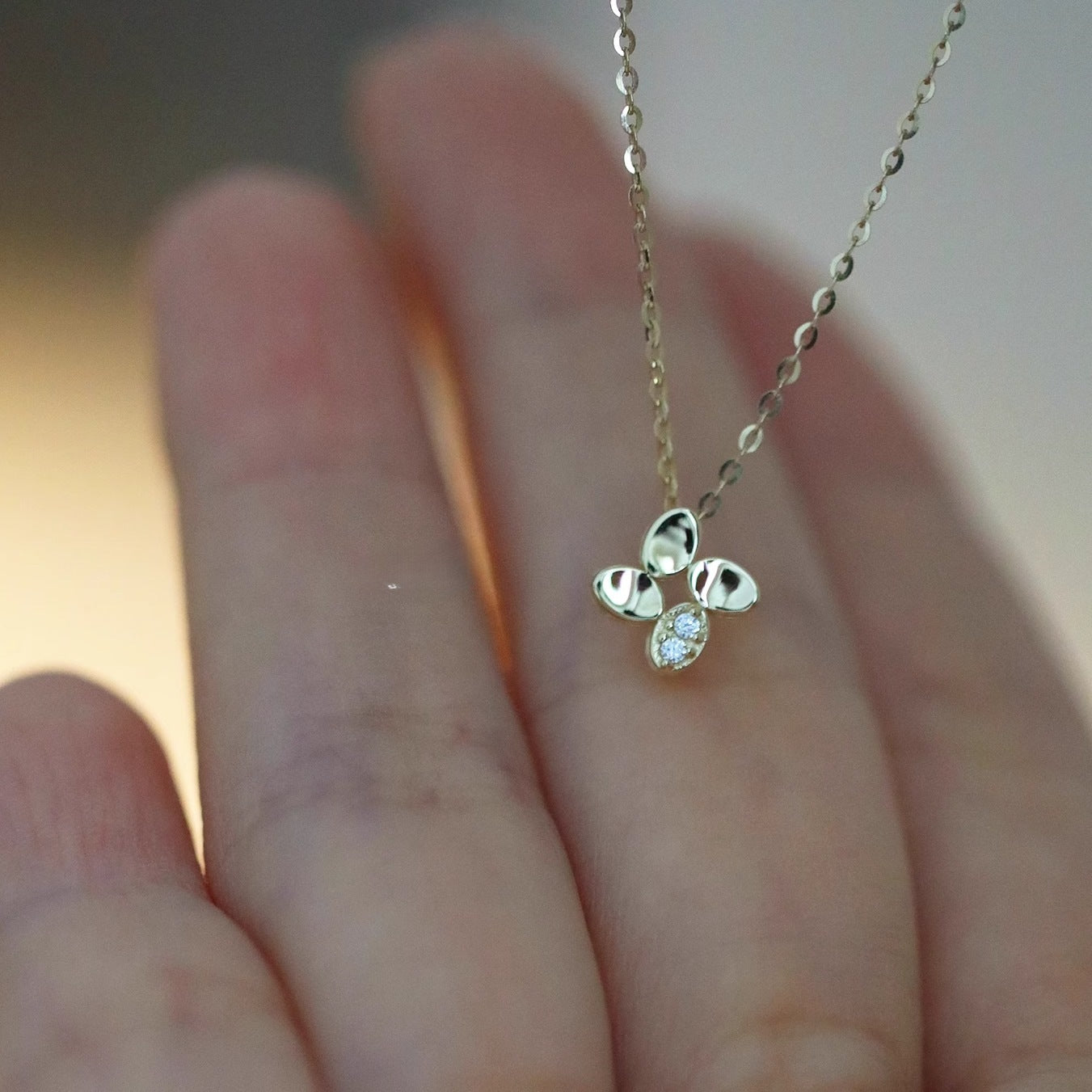 Hand holding lucky four leaf flower pendant necklace, 14K gold plated 925 sterling silver, wholesale jewelry for everyday wear.
