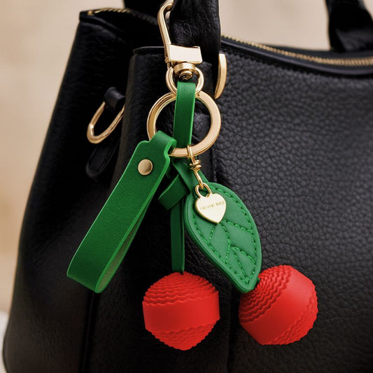 Cherry keychain red leather bag charm with green leaf and gold clasp attached to black handbag – cute fruit keyring for bags