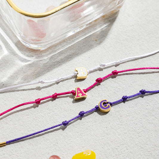 Close-up of gold stainless steel initial bracelets featuring A, B, C enamel letters. These adjustable friendship bracelets are perfect for bulk orders and wholesale initial jewelry for boutique gifting.