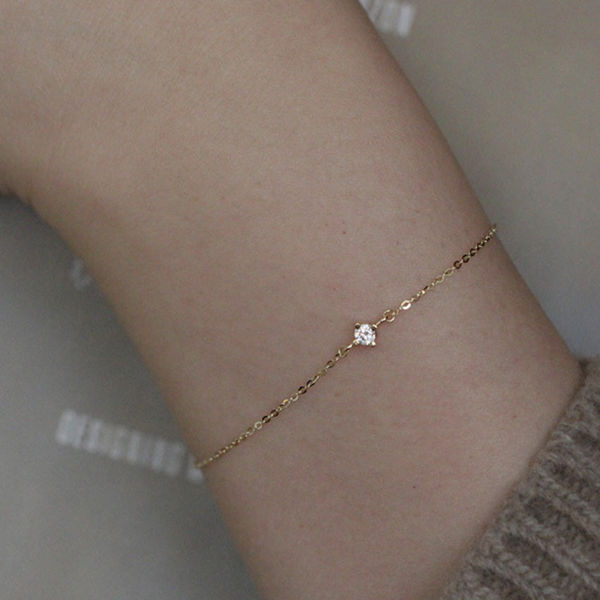 Close up of delicate 14k gold plated silver chain bracelet with single cubic zirconia stone on model wrist
