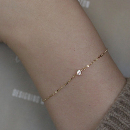 Close up of delicate 14k gold plated silver chain bracelet with single cubic zirconia stone on model wrist