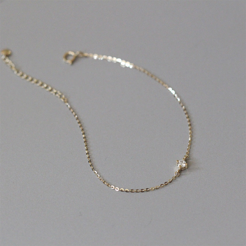 Dainty gold cz solitaire bracelet laid flat on gray surface showing delicate link chain and clasp for bulk buyers