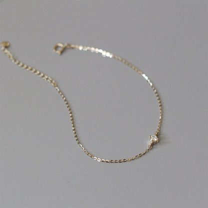 Dainty gold cz solitaire bracelet laid flat on gray surface showing delicate link chain and clasp for bulk buyers