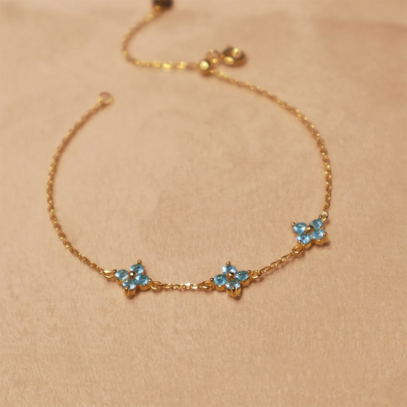 Flat lay of 18k gold plated silver clover bracelet with blue cubic zirconia stones