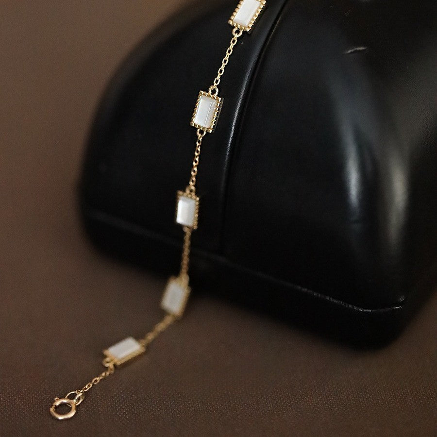 Full layout of mother of pearl gold chain bracelet with adjustable clasp on dark wood surface for wholesale jewelry buyers