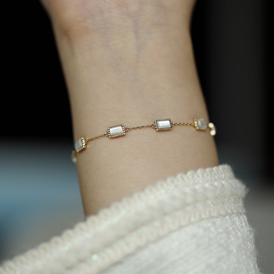 Elegant gold chain bracelet with rectangular mother of pearl links draped over a black stand for retail merchandising