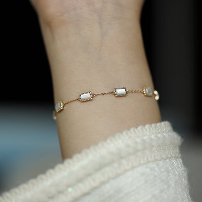 Elegant gold chain bracelet with rectangular mother of pearl links draped over a black stand for retail merchandising