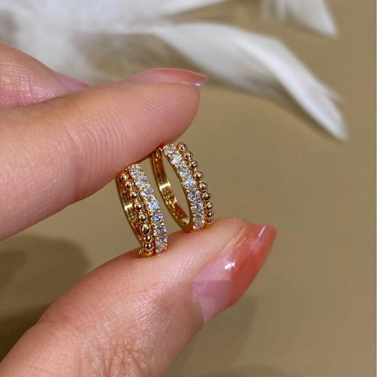 Hand holding two 18k gold plated cubic zirconia beaded huggie hoops, 925 sterling silver earrings wholesale supplier.
