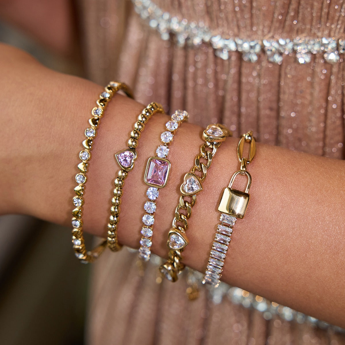 A layered wrist stack with gold and stainless steel pink tennis bracelets, featuring pink cubic zirconia hearts and stones, highlighting romantic valentines jewelry for her and trendy wholesale fashion accessories.
