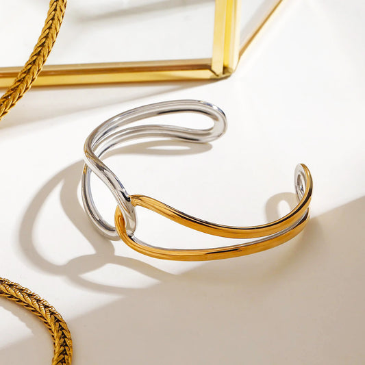 Minimalist stainless steel bangle in two tone gold and silver finish, captured under soft lighting, reflecting the modern elegance of dark feminine style accessories.