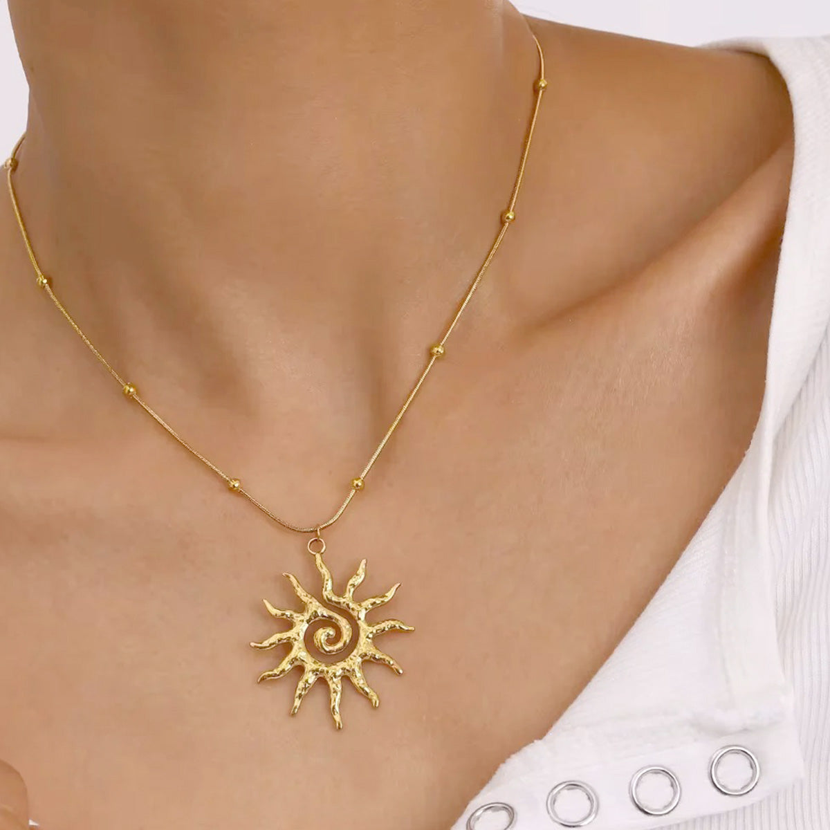 Flat lay of boho-style gold necklaces on sand, including sun pendant necklace and matching beach-themed 18k gold plated stainless steel pieces.