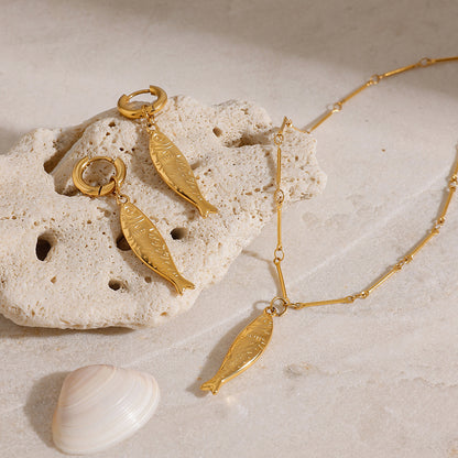 Close-up of 18k gold plated earrings with fish pendants, part of a stainless steel matching jewelry set. Perfect for summer beach jewelry or vacation jewelry looks.