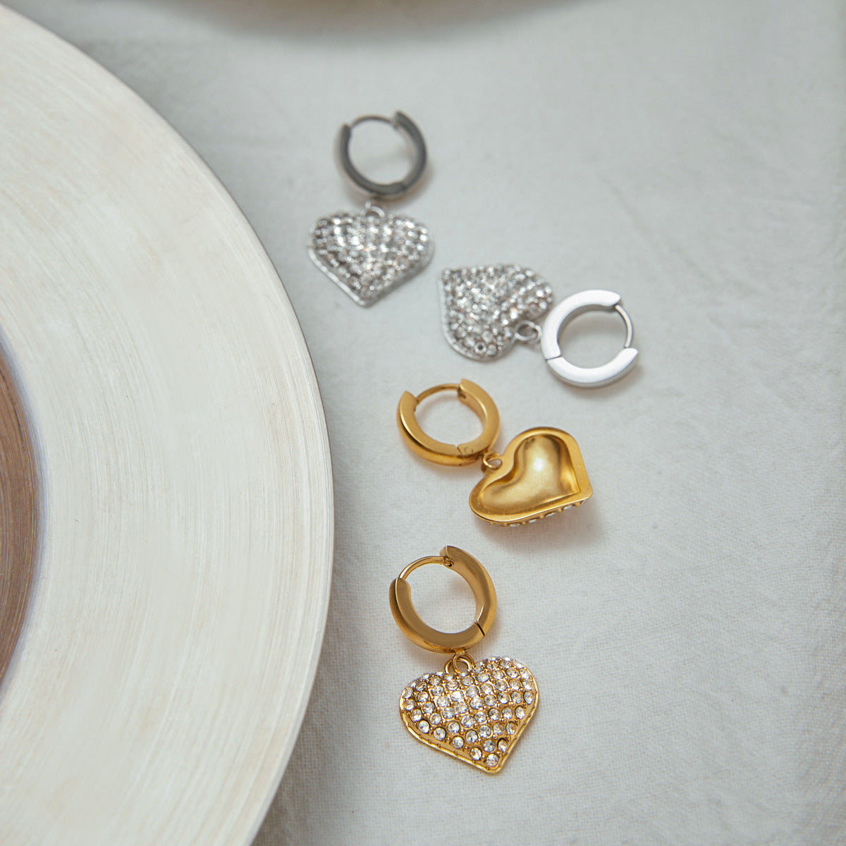 Close-up of PVD gold plated heart zircon drop hoop earrings styled with other stainless steel jewelry. These women's costume jewelry earrings make great additions for wholesale catalogs and boutique displays.