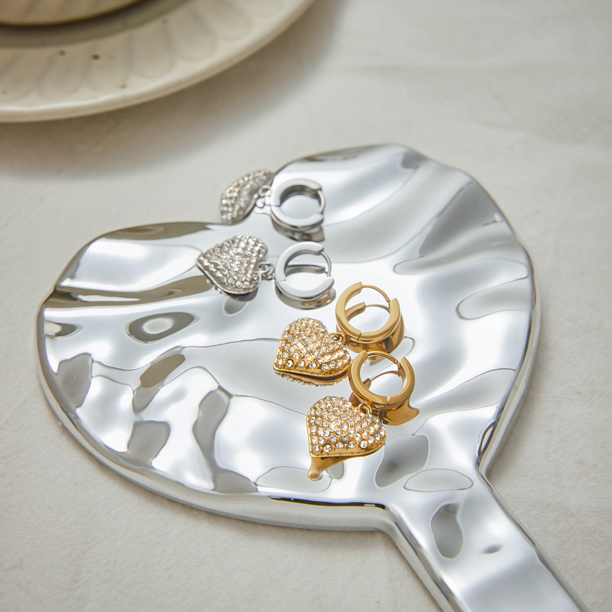 Gold and silver heart zircon earrings for women arranged on a modern serving plate. These drop hoop earrings in stainless steel are fashionable and non-tarnish, ideal for wholesale jewelry suppliers and gift shops.