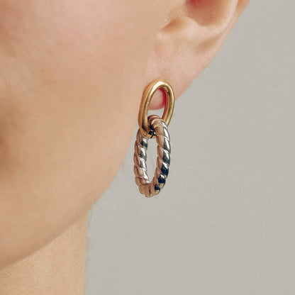 Model wearing chunky oval twist earrings in gold and silver. Two tone stainless steel earrings perfect for women seeking geometric jewelry with hypoallergenic titanium studs. Ideal for wholesale fashion accessories.