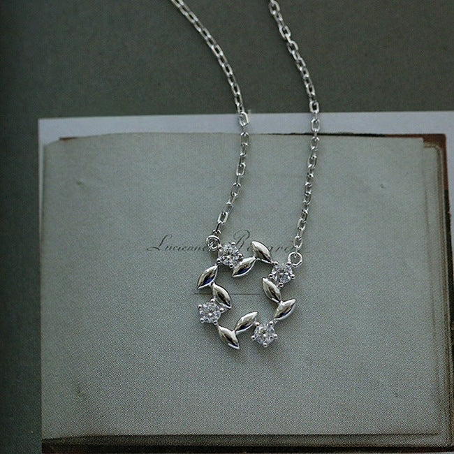 Close view of 14K gold plated leaf wreath zircon pendant necklace on book page