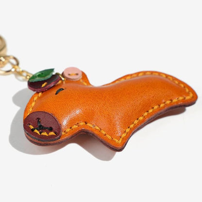 Detailed side view of orange leather capybara keychain accessory with decorative fruit element for bags or keys