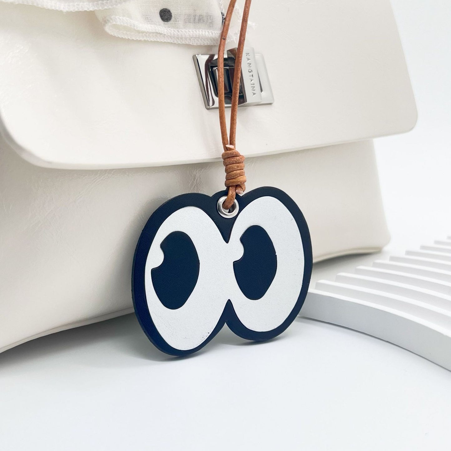 Front close-up of leather bag charm with cartoon eyes graphic attached to a white purse