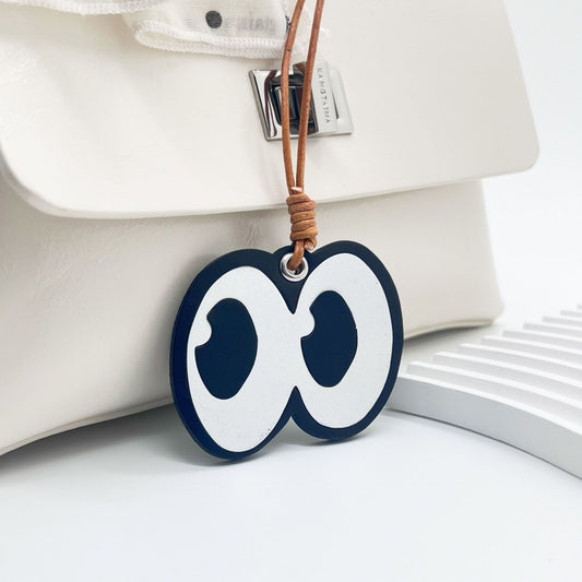Front close-up of leather bag charm with cartoon eyes graphic attached to a white purse