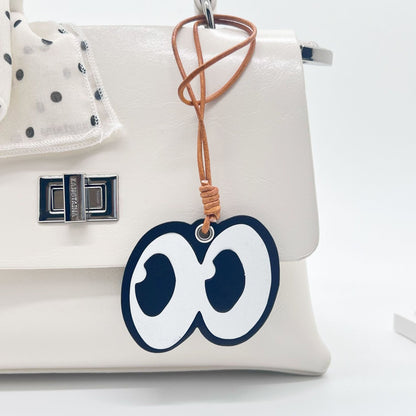 Cartoon eyes design leather bag charm hanging from a white handbag with tan leather cord