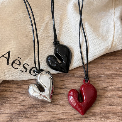 Three chunky heart pendant necklaces in black, silver, and red laid flat on fabric.