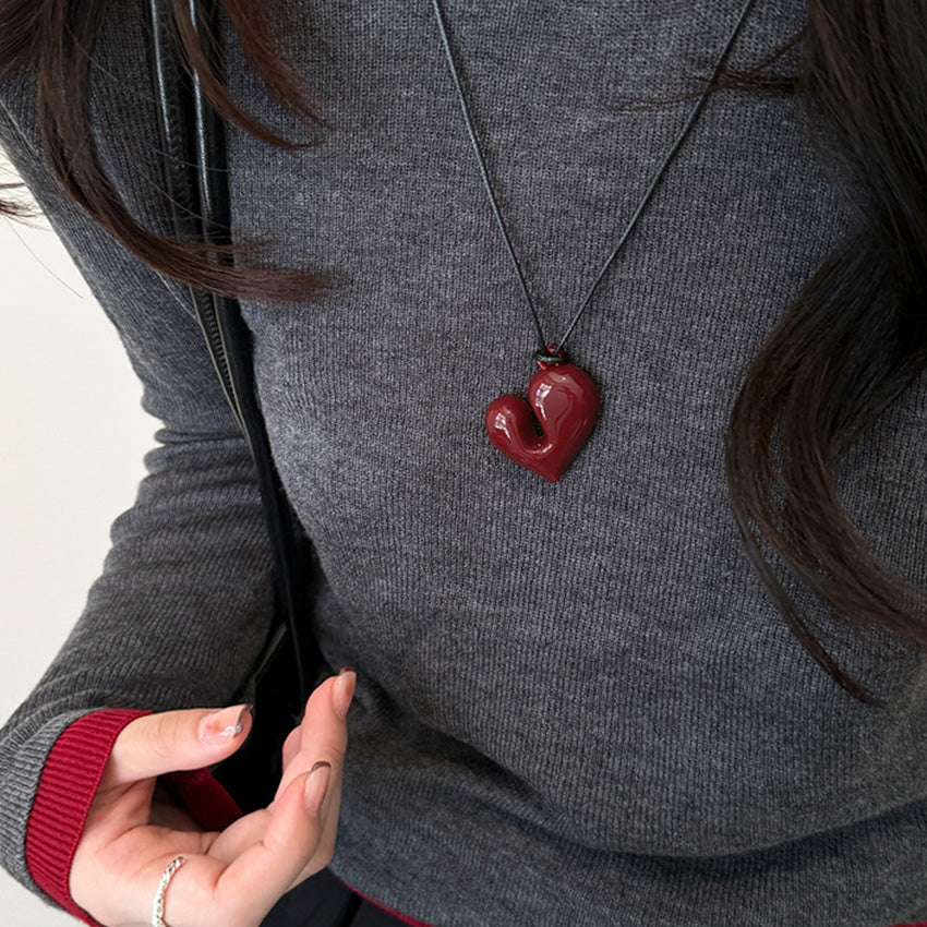 Woman wearing a red chunky heart pendant necklace over a grey sweater.