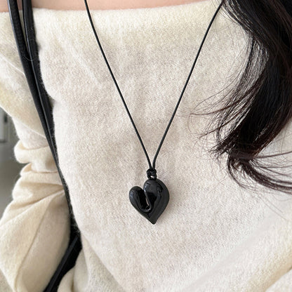 Black chunky heart necklace worn with an off-shoulder cream top.
