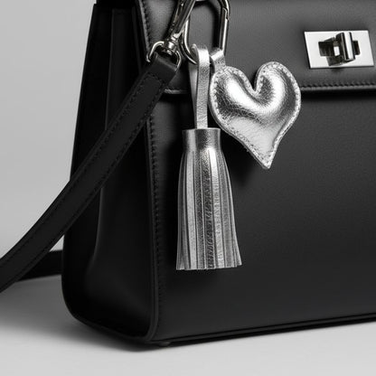 Metallic silver leather heart keychain with matching tassel on black handbag.