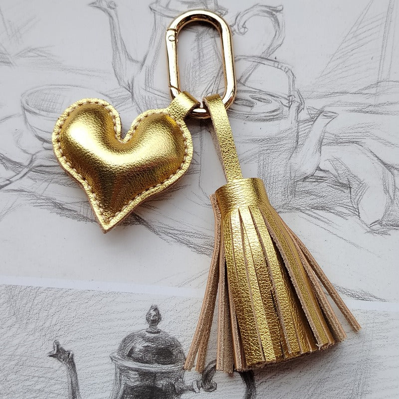 Gold leather heart keychain with tassel charm displayed on sketchbook background.