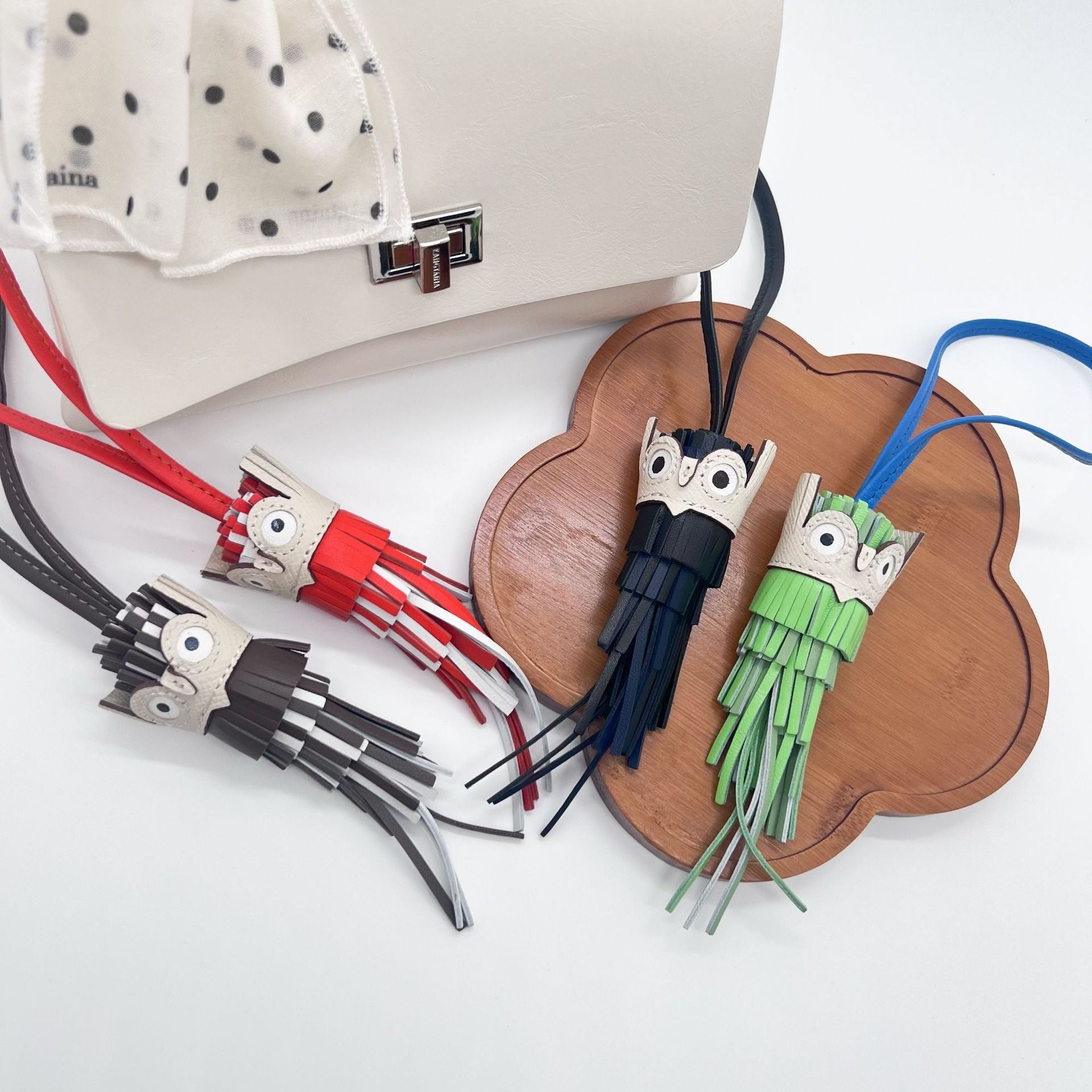 Colorful leather owl keychains with tassel charm displayed on bag and tray