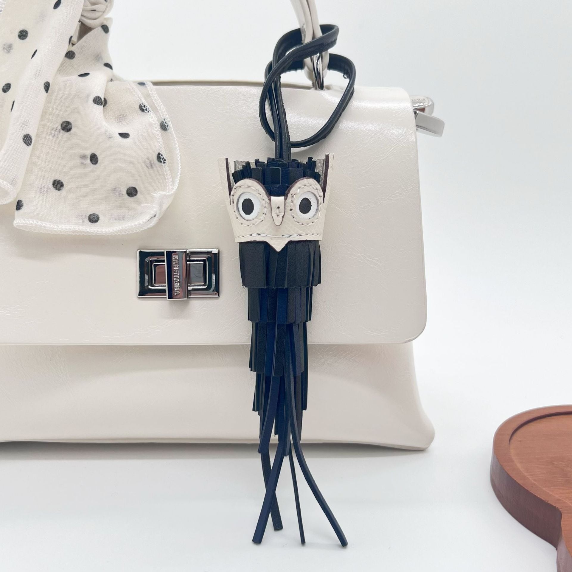 Black leather owl keychain with tassel charm hanging on white handbag
