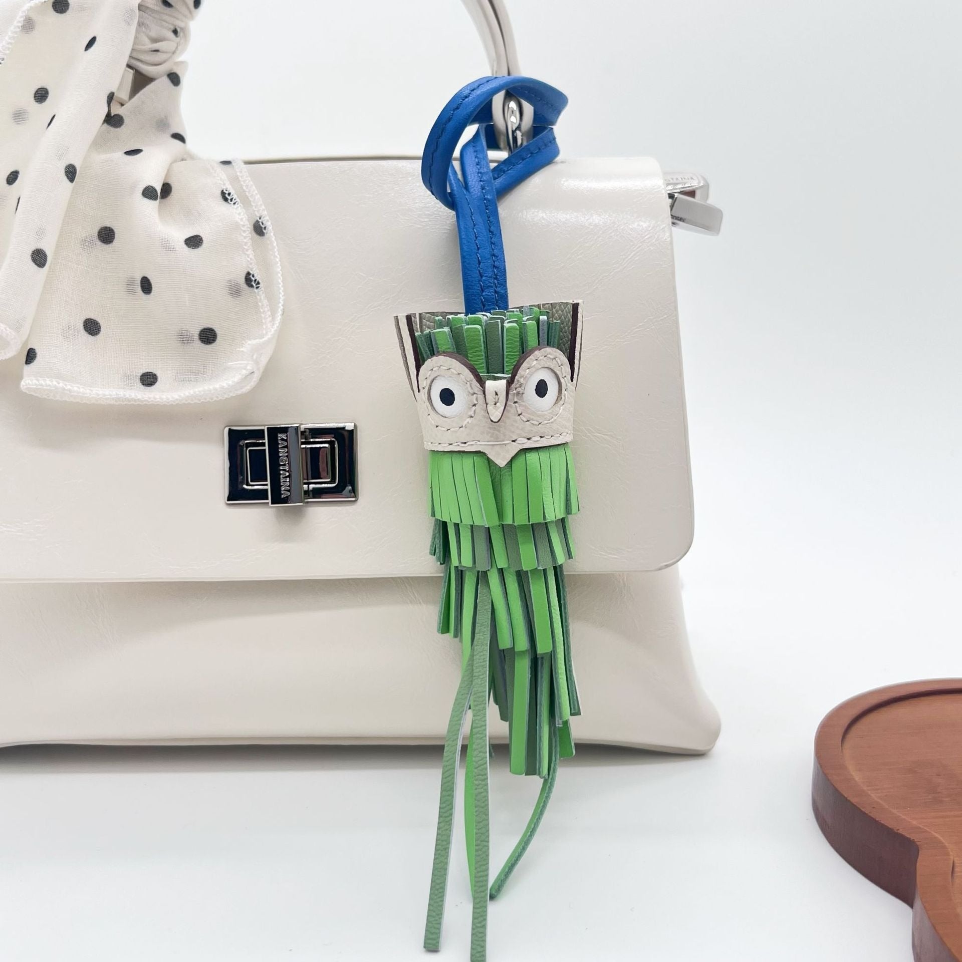 Green and blue leather owl tassel charm keychain hanging on white handbag